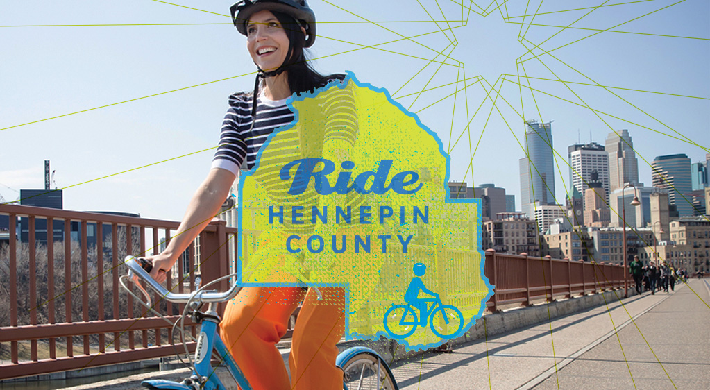 Ride Hennepin County. Photo of a woman riding her bike along a bridge near downtown Minneapolis.