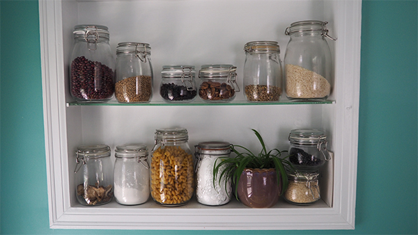 variety of sizes of glass jars with food inside on two shelves in a wall
