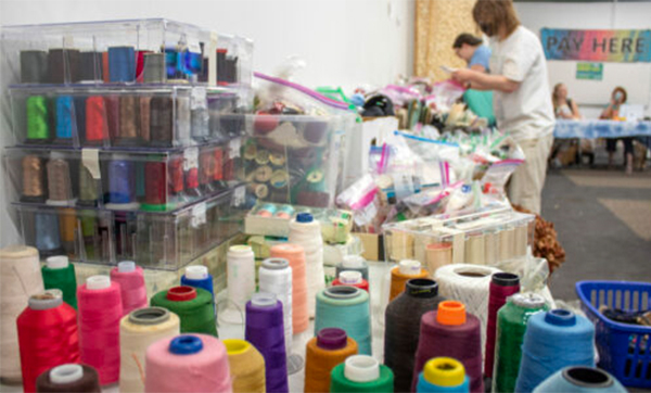 various colored large spools of thread with shoppers in the background