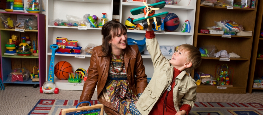 Boy playing with wooden plane toy while mom watches