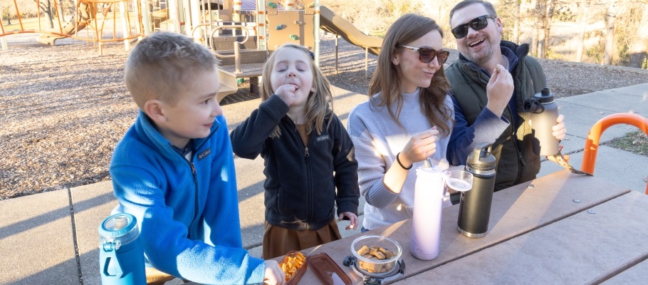 Family at a picnic table eating snacks from reusable containers