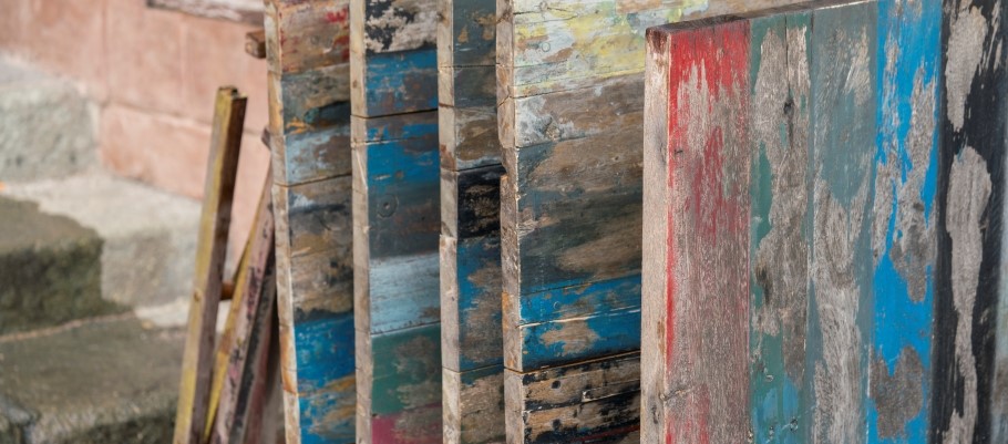 A collection of aged wood scraps, showing signs of peeling paint in multiple hues, arranged in a messy pile.