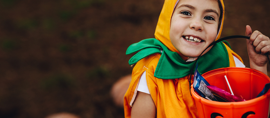Kid smiling in costume holding candy bucket