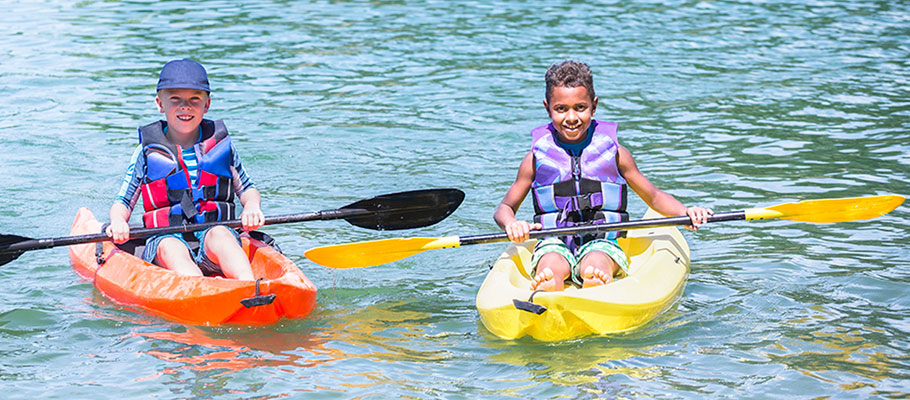 Two kids paddling kayaks and smiling