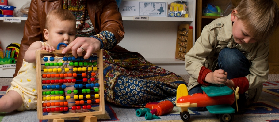 Baby plays with wooden abacus while mom watches