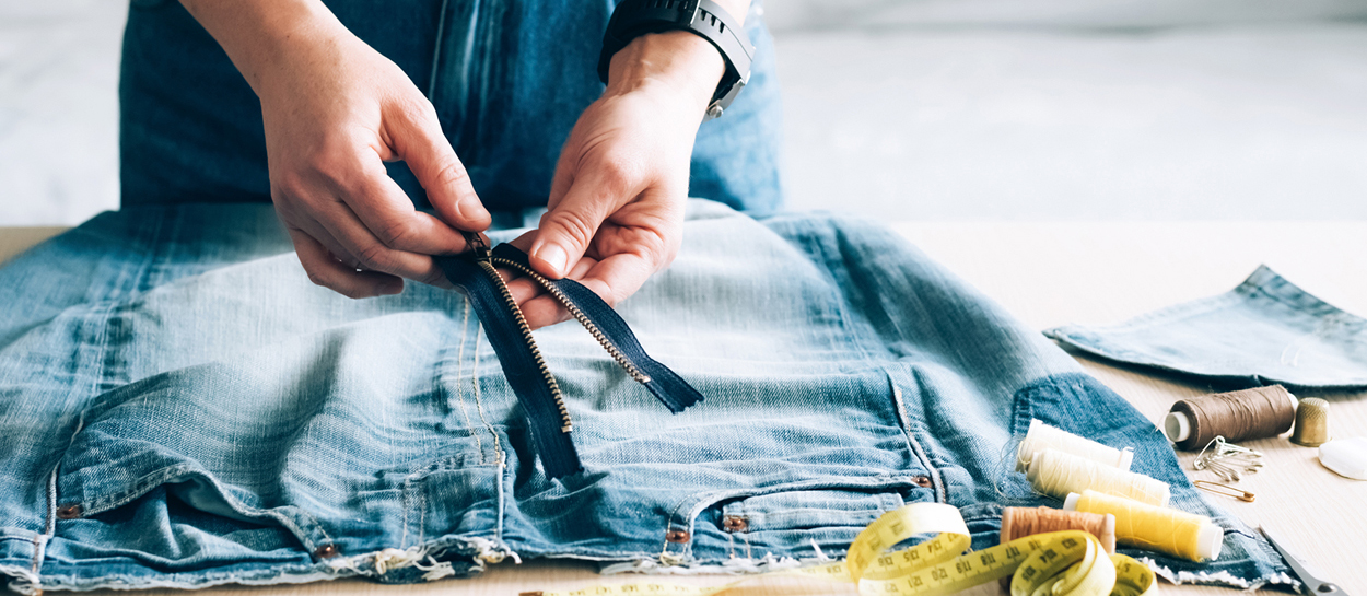 Close up of hands mending a zipper on jeans