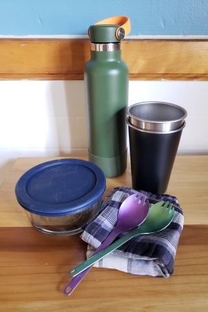 Reusable water bottle, coffee mug, Tupperware, silverware, and napkin