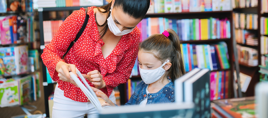 Mother and daughter wearing masks looking at a used book