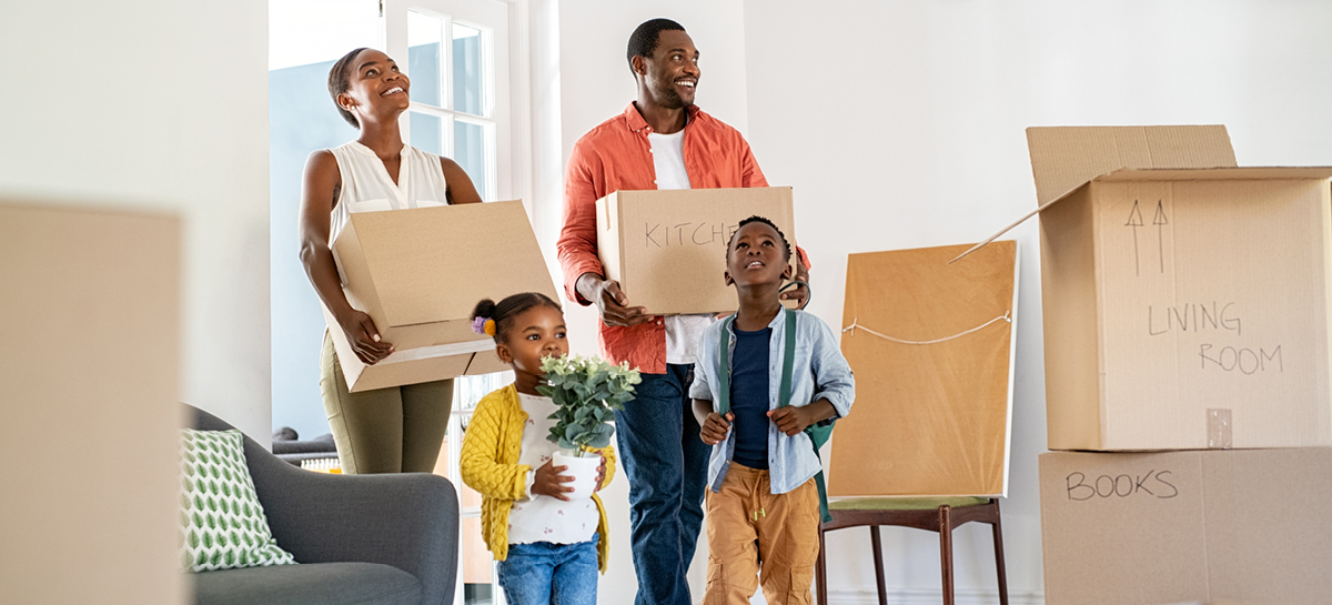 Family with two young children carrying boxes into their new home