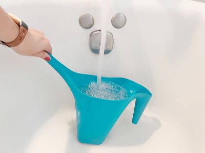 Watering container held under running bathtub faucet