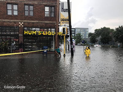 People walking through waste-deep floodwaters on Lyndale Avenue outside of Hum's Liquor
