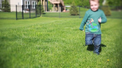 Small boy wearing shirt with bike with planet earth wheel running on green lawn