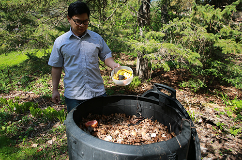 Man adding food scraps to compost bin full of leaves