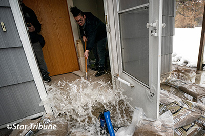 Person sweeping water out of flooded house, photo credit Star Tribune