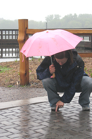 Woman holding umbrella looking at rain falling on porous pavement