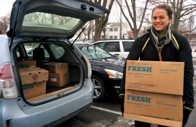 Woman holding boxes of rescued food by open car trunk