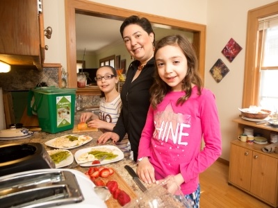 Family chopping vegetables in kitchen and putting food scraps in organics bin