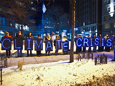 Line of people in dark holding light up signs that say climate crisis