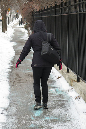 Woman walking carefully on ice covered sidewalk sprinkled with salt