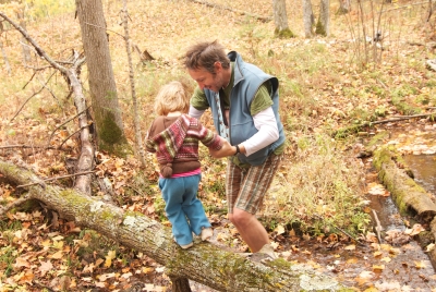 Man helping young boy cross fallen log in autumn forest