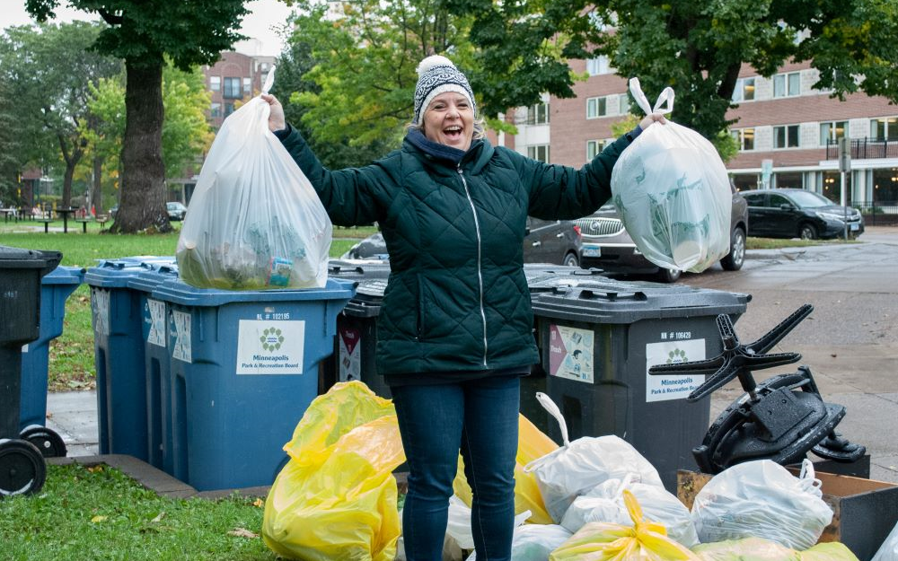 Woman triumphantly holding up two bags of litter during clean up event.