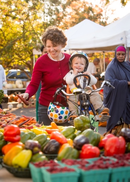 Mother with child in stroller looking at vegetables at market.