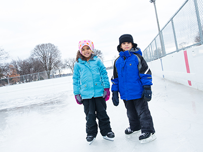Two kids bundled up standing on skating rink