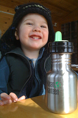 Молодой мальчик пьет из многоразовой бутылки с водой