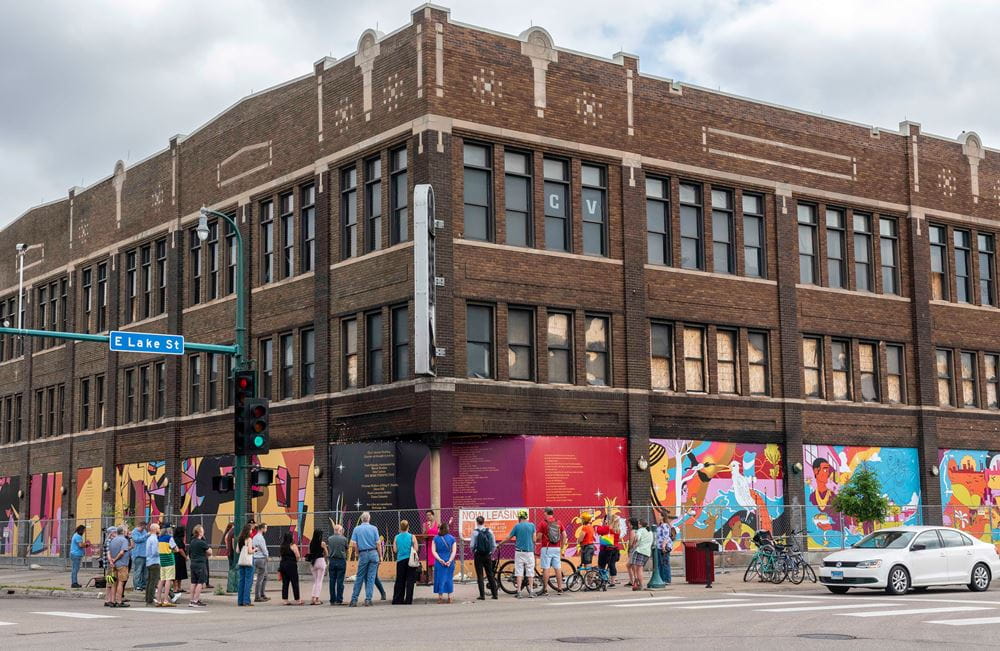 The coliseum building with murals around the ground floor and people standing out front
