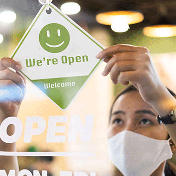 Masked woman hanging a "we're open" sign in the window