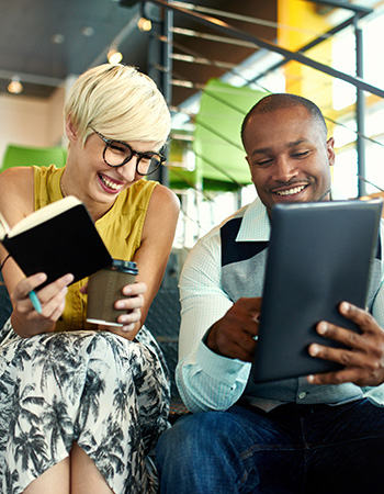 Two coworkers laugh in an office setting. 
