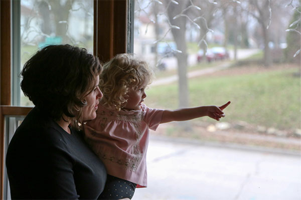 mom and daughter looking out the window of their home